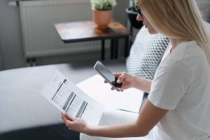 A woman looking at a smart phone and a paper document