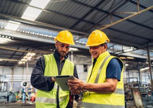 Workers with hard hats and safety vests using a tablet